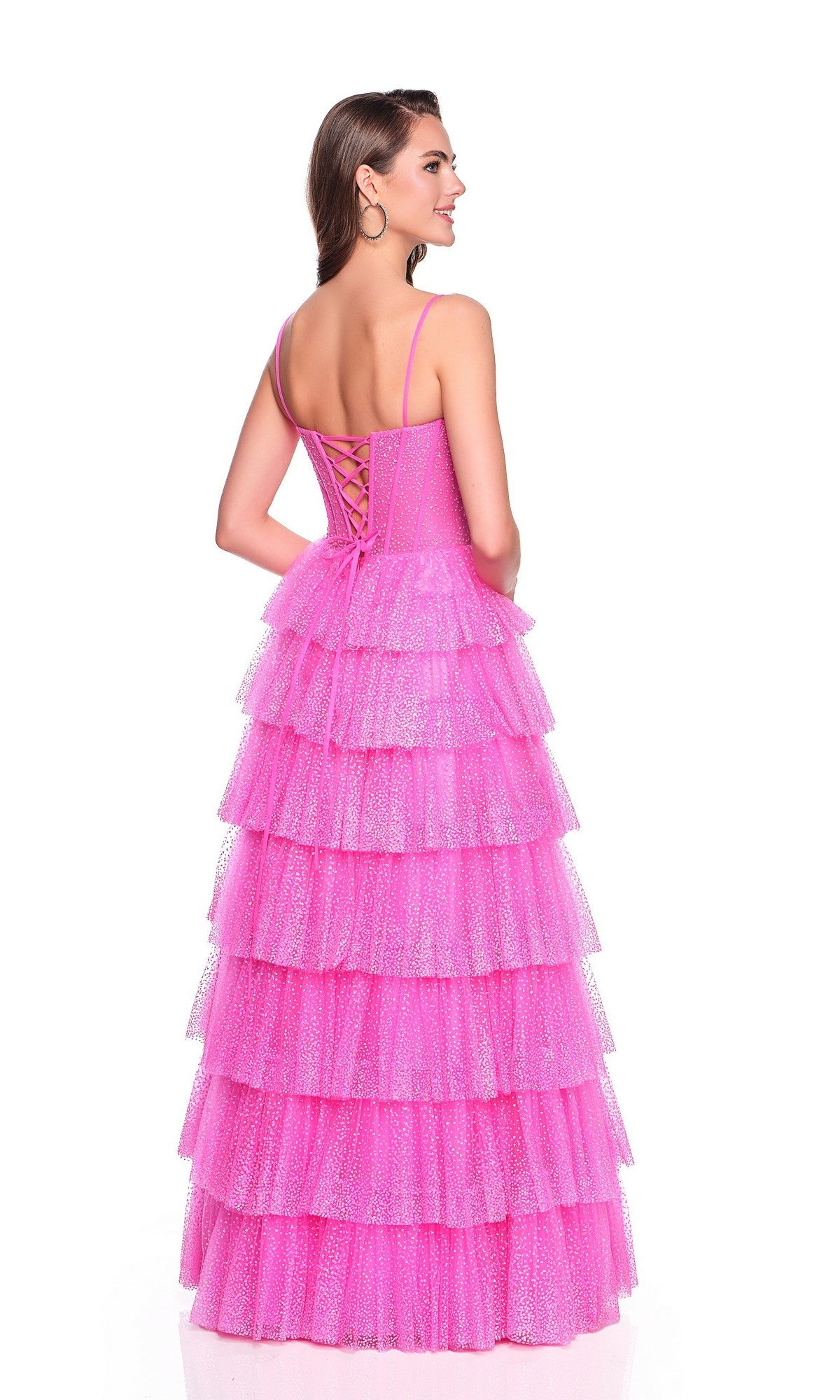 Woman wearing the Long Prom Dress: Dave and Johnny 12397, a sleeveless fuchsia pink gown with a tiered ruffle glitter tulle skirt and lace-up corset bodice, standing and smiling against a white background.